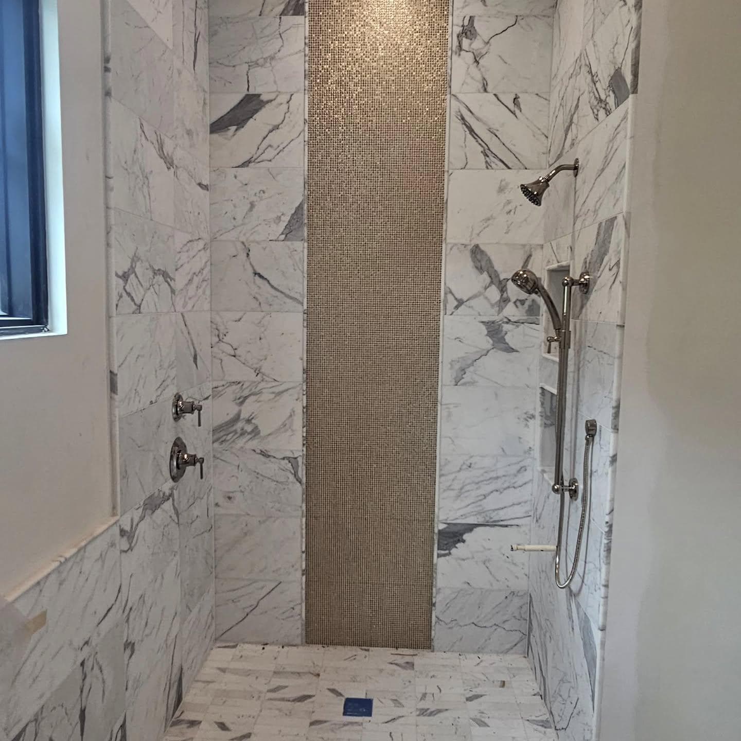 Marble tile shower with vertical gold mosaic accent strip