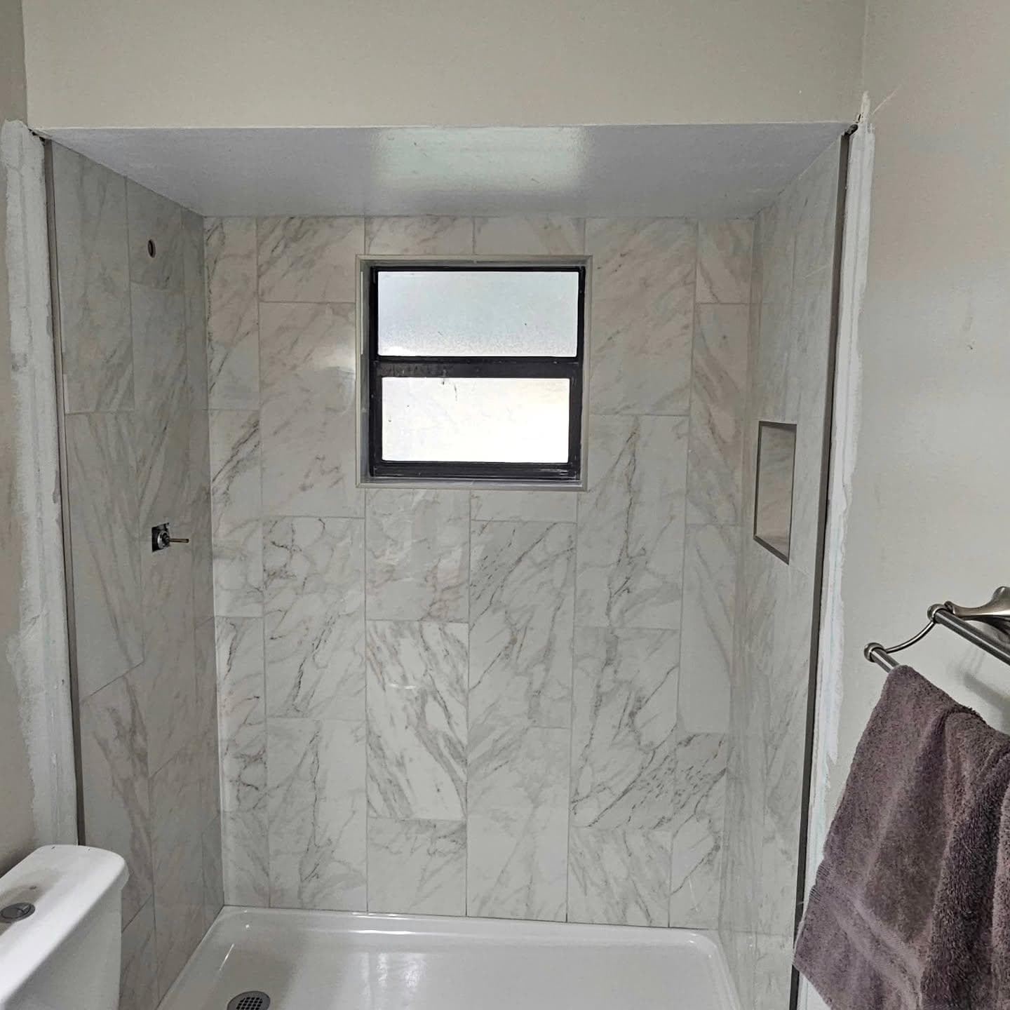 Marble tile shower with natural light window and niche